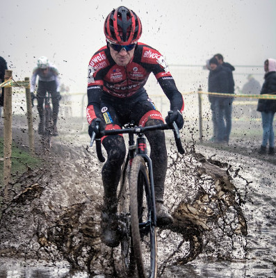 man riding bycicle competitively through mud