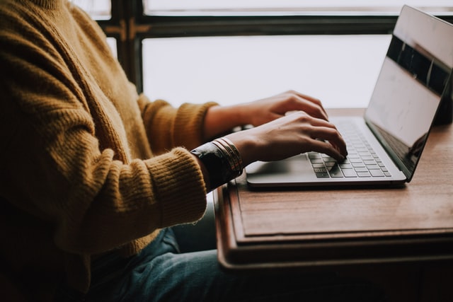 Person seated behind computer with mustard color sweater