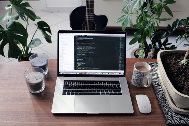 Computer on desk with code editor open, candles around it and coffee mug